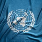 UN Ambassador’s Double Life Exposed United Nations flag featuring a world map and olive branches on a blue background