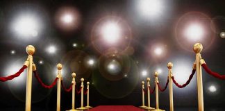 A red carpet lined with gold stanchions and ropes under bright spotlights