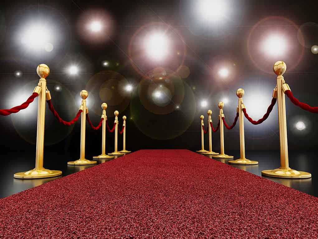 A red carpet lined with gold stanchions and ropes under bright spotlights
