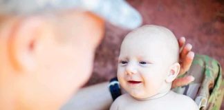 A smiling baby interacting with a parent in a military uniform