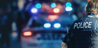 Gunman WOUNDS Cop — Manhunt Shuts Down Town Police officer with patrol car and flashing lights.