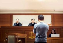 Man stands in courtroom before judges and stenographer.