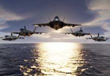 Five jets flying low over the ocean at sunset.