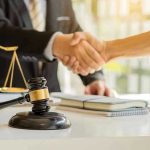 Hands shaking over legal documents with gavel and scales.