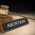 Gavel and sign reading Abortion on a wooden surface.