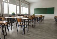 Empty classroom with desks, chairs, windows, and chalkboard.
