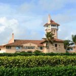 Large pink mansion with tower, palm trees, and garden.