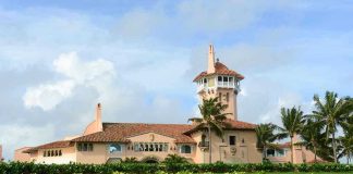 Large pink mansion with tower, palm trees, and garden.