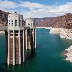 Grenade-Like Device Found in a Dam – Who Did It? A large dam structure with two towers over a blue water reservoir surrounded by rocky mountains