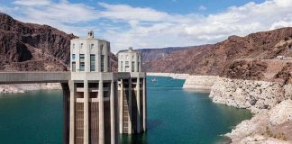 Grenade-Like Device Found in a Dam – Who Did It? A large dam structure with two towers over a blue water reservoir surrounded by rocky mountains