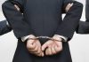 A person in a suit with hands cuffed behind their back