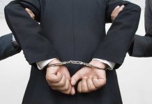 A person in a suit with hands cuffed behind their back
