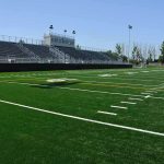 Incredible Season Shakes Up European Football A football field with artificial turf and empty bleachers under a clear blue sky