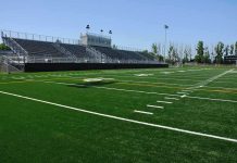 A football field with artificial turf and empty bleachers under a clear blue sky