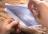 A hand holding an envelope containing a check on a wooden table