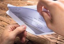 A hand holding an envelope containing a check on a wooden table
