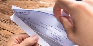 A hand holding an envelope containing a check on a wooden table