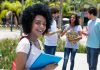 Student smiling with folders outdoors near classmates