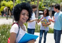 Student smiling with folders outdoors near classmates
