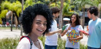 Student smiling with folders outdoors near classmates