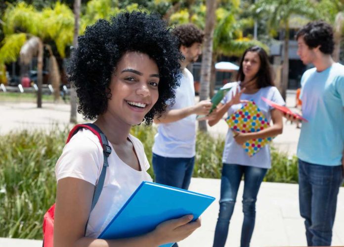 Student smiling with folders outdoors near classmates