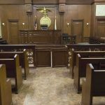 Kill Threat Ignites DOJ Minefield Interior view of an empty courtroom with wooden benches and a judges bench