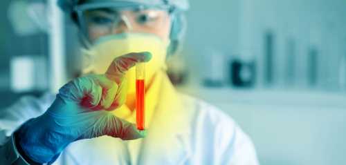 Scientist holding a test tube with red liquid in a laboratory setting