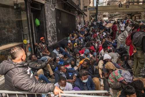 shutterstock_2346880441 A large group of people sitting on a city street, some wearing masks