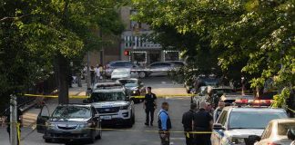 Police officers secure a residential street with patrol cars and yellow tape