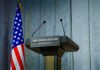 Press podium with the White House sign and an American flag in the background