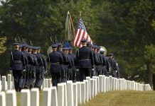 Military honor guard marches through a cemetery with flags