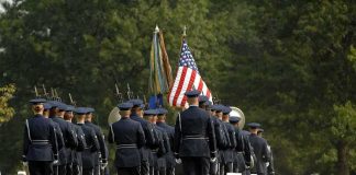 Military honor guard marches through a cemetery with flags
