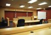 Interior view of an empty courtroom with wooden furniture and American flags