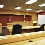 From Chart-Topping Star to Murder Trial Interior view of an empty courtroom with wooden furniture and American flags