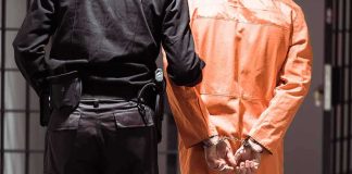 Prisoner in orange jumpsuit handcuffed with guard standing beside