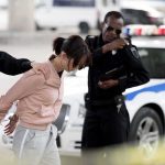 Police officers detain a woman beside a patrol car