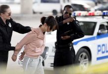 Police officers detain a woman beside a patrol car