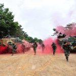 Soldiers running with armored vehicles through red smoke
