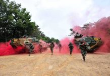 Soldiers running with armored vehicles through red smoke