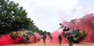 Soldiers running with armored vehicles through red smoke