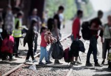 People with bags walking along railway tracks