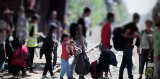 People with bags walking along railway tracks