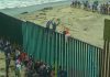 People climbing a tall beachside border fence