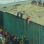 People climbing a tall beachside border fence