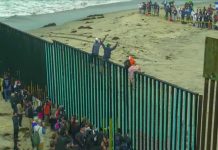 People climbing a tall beachside border fence