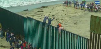 Ceuta Declares Health Emergency as Migrant Centers Collapse People climbing a tall beachside border fence