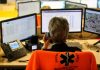 Emergency dispatcher at workstation with multiple monitors and phone