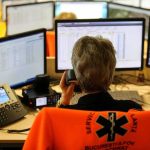 Emergency dispatcher at workstation with multiple monitors and phone