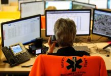 Emergency dispatcher at workstation with multiple monitors and phone