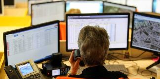 Emergency dispatcher at workstation with multiple monitors and phone